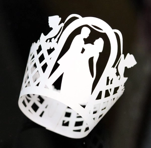Detail of laser-cut white wedding cupcake wrapper featuring romantic silhouettes