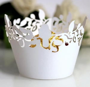 Macro shot of white laser-cut cupcake wrapper with bird and vine patterns for weddings