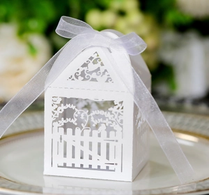 Detailed laser-cut white favor box with house shape, fence pattern, and ribbon