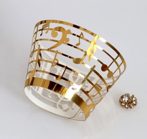 Detail of laser-cut gold musical note cupcake wrapper with elegant staff patterns