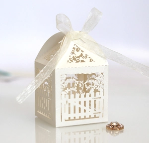 Detail of white laser-cut wedding favor box with intricate garden fence and bird pattern