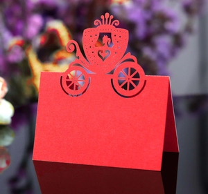 Macro detail of red laser-cut pumpkin carriage wedding place cards on reflective surface