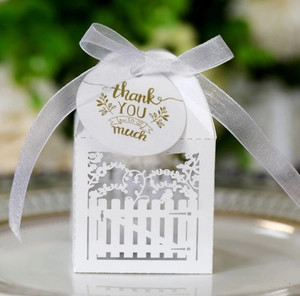Macro detail of white laser-cut garden fence candy box with gold thank you tag and ribbon