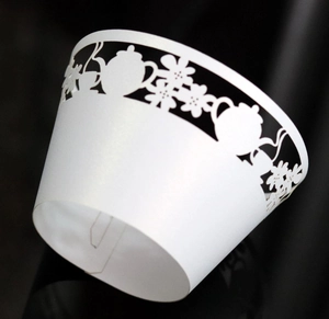 Macro detail of white laser-cut cupcake wrappers with elegant teapot and floral pattern