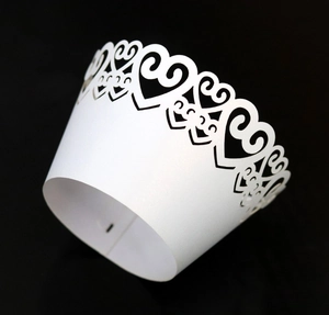 Detail view of laser-cut white heart cupcake wrapper with intricate scroll patterns