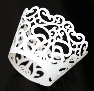 Close-up of white laser-cut floral scroll cupcake wrapper with elegant hollowed pattern