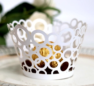 Elegant white laser-cut cupcake wrappers with overlapping circle patterns and wavy edges