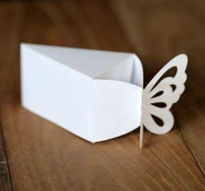 Macro detail of white triangle paper wedding favor box with hollow butterfly design