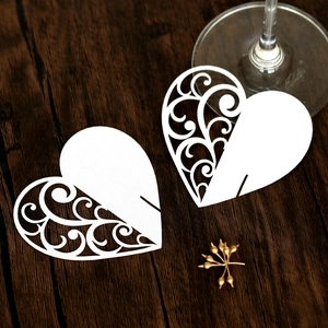 Detailed view of white heart-shaped laser-cut wine glass cards on a wood surface
