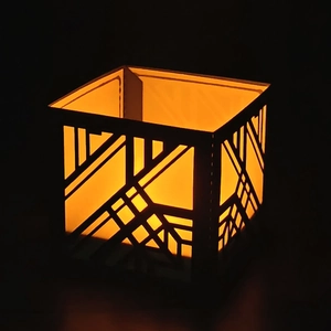 Detail of black geometric laser-cut paper lampshade with warm orange glowing light effect