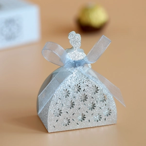 Detail of silver glitter dress-shaped candy box with hollow floral patterns and blue ribbon bow