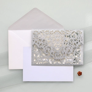 Detailed silver glitter laser-cut invitation set with vine patterns and white envelope