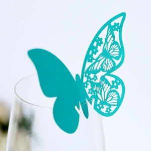 Macro shot of teal butterfly place card with delicate laser-cut floral wing on glass rim
