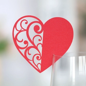 Detailed macro view of laser-cut red heart wine glass card for wedding table decoration