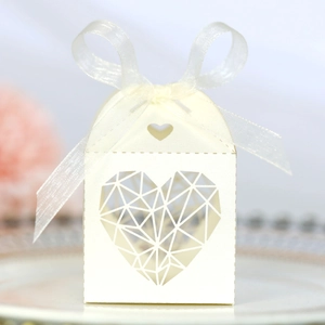 Détail de boîte à dragées ivoire avec cœur ajouré et ruban blanc pour cadeaux de mariage