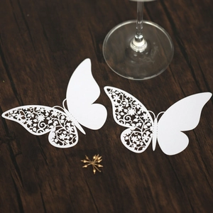 Detail of white laser-cut butterfly place cards with floral patterns on wood surface
