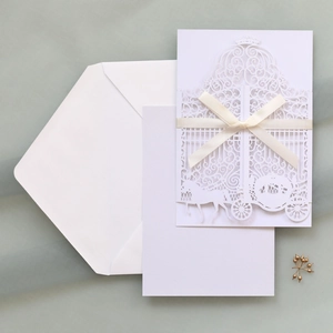 Detailed laser-cut white wedding invitation set with carriage motif and cream ribbon