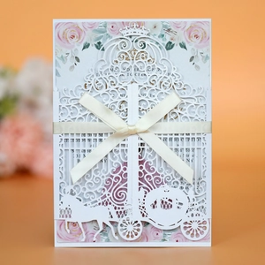 Detail of laser-cut wedding invitation featuring a white pumpkin carriage and beige ribbon
