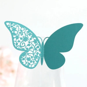 Detail of laser-cut teal paper butterfly with floral hollow pattern for wine glasses