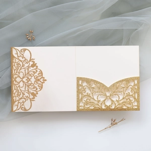 Macro shot of laser-cut glitter patterns and floral details on cream wedding invitations