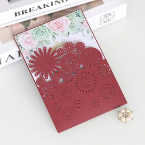 Close-up of laser-cut burgundy wedding invitation with floral insert and pearl buckle