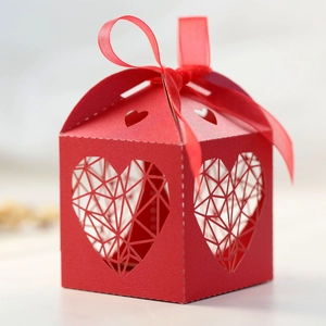 Détail d'une boîte cadeau rouge ajourée avec cœur découpé et ruban en soie assorti