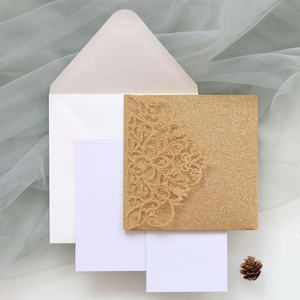 Macro detail of laser-cut floral pattern on golden glitter wedding invitation cards