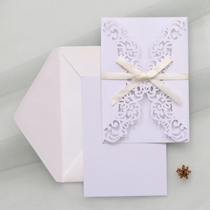 Detail of laser-cut floral wedding invitation with cream ribbon bow and matching envelope