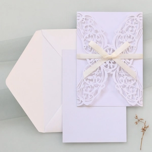 Detailed laser-cut invitation set with cream cover, white insert card, and silk ribbon