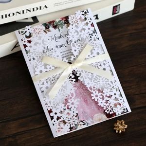 Detail of laser-cut wedding invitation with cream satin bow and floral inner page