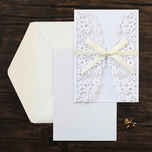 Laser-cut floral wedding invitation with cream ribbon on dark wooden background