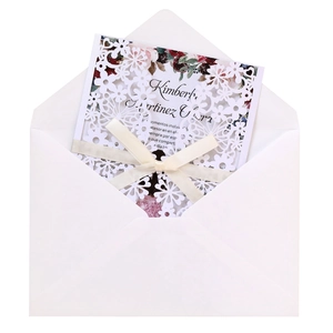 Close-up of laser-cut floral wedding invitation with cream ribbon bow and printed insert