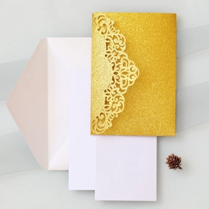 Close-up of laser-cut glitter gold wedding invitation with white envelope and cards