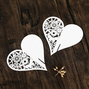 Detailed laser-cut heart place cards with white lace patterns on a wooden surface