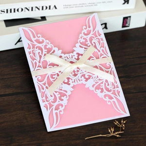 Detail view of laser-cut wedding invitation with pink cardstock and cream satin ribbon bow