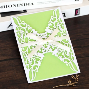 Close-up of laser-cut wedding invitation with green cardstock and cream satin ribbon