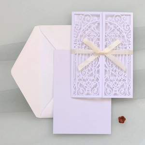 Detail of laser-cut wedding invitation with white floral lace cover and silk bow decoration