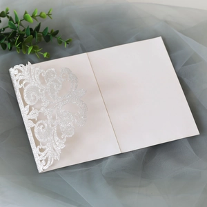 Detail of silver glitter laser cut invitation with intricate floral lace and white card