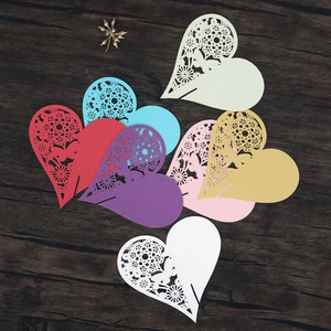 Detail of laser-cut heart place cards with lace patterns on dark wood background