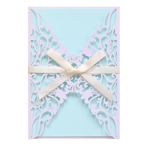 Macro shot of laser cut flower pattern on white wedding invitation with blue ribbon