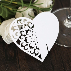 Close-up of laser-cut white heart card for wedding glasses on a rustic wooden table