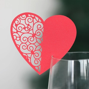 Detailed laser-cut scrollwork on red heart-shaped paper wine glass card for parties