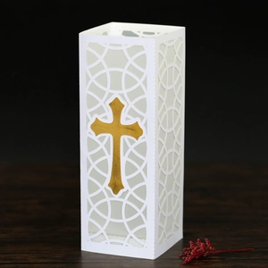 Detailed laser-cut white paper candle lantern with a gold cross and hollow patterns
