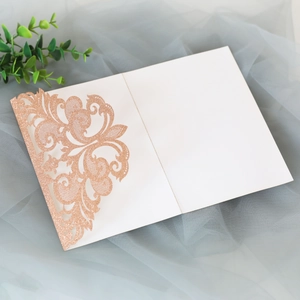 Detailed close-up of rose gold laser-cut lace floral invitation with glitter texture