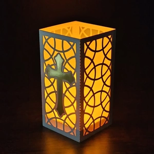 Detailed view of white hollow cross lantern with warm yellow light on wood table