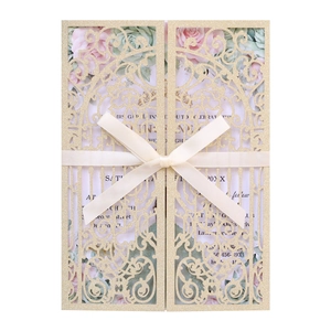 Macro detail of laser-cut glitter gold wedding invitation with ribbon and floral print