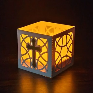 Detail showing laser-cut cross patterns on a white candle paper lantern with warm light