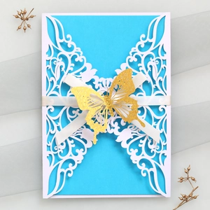 Detail of laser-cut invitation with blue card, white floral lace, and gold glitter butterfly