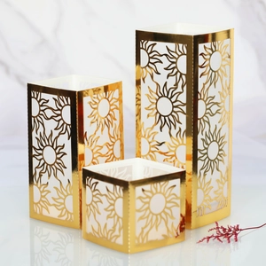 Three-piece gold paper candle covers with laser-cut sun patterns on marble surface