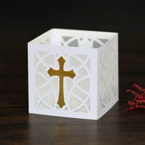 Detail of laser-cut white paper lantern with gold cross on dark wood background